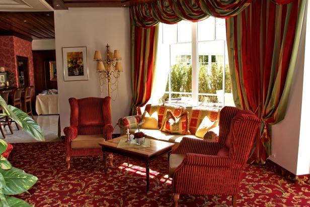 Ein Wohnzimmer mit roten Sesseln, einem Sofa und einem Fenster mit Vorhängen.