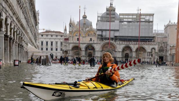 Eine Frau paddelt mit einem Kajak durch das Hochwasser auf dem Markusplatz in Venedig.