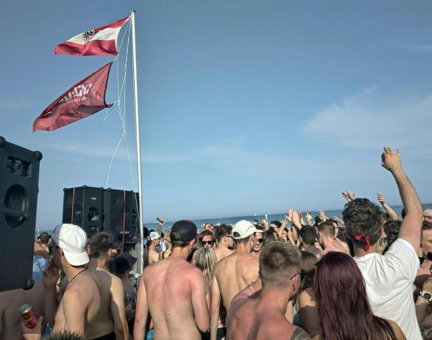 Eine Menschenmenge feiert am Strand unter einer österreichischen Flagge.