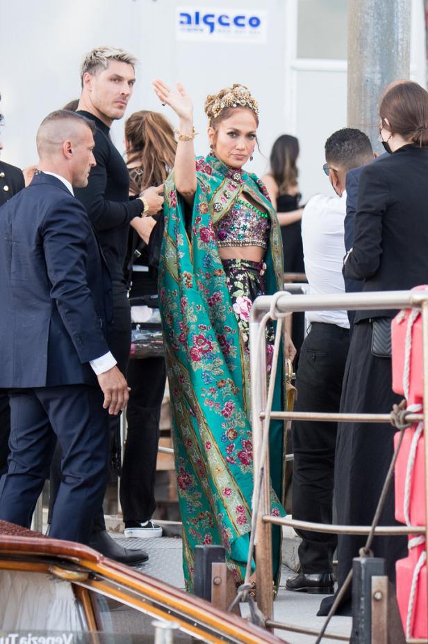 Jennifer Lopez trägt ein blumengemustertes Cape und winkt.