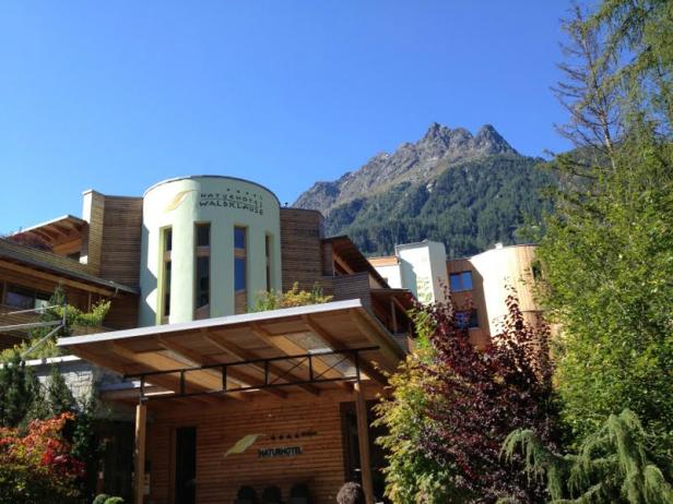 Das Naturhotel Waldklause vor einer Bergkulisse an einem sonnigen Tag.