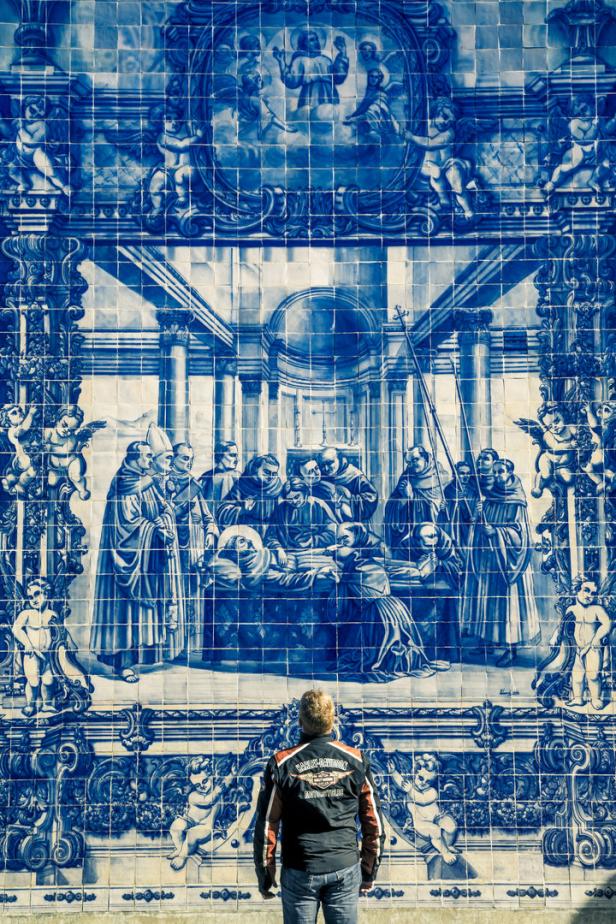 Ein Mann betrachtet ein blaues Azulejo-Wandbild mit religiöser Szene.