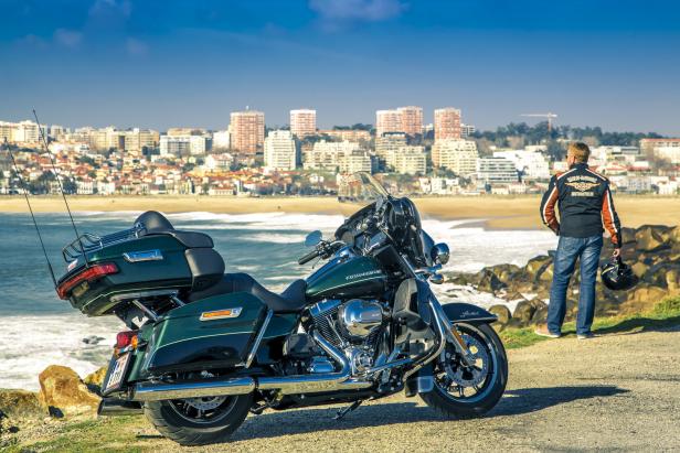Ein Mann steht neben seiner Harley-Davidson mit Blick auf den Strand und die Stadt.