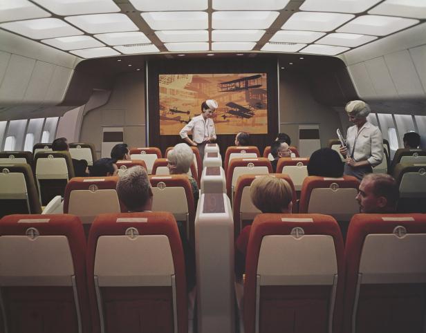 Zwei Stewardessen präsentieren vor Passagieren ein Bild von historischen Flugzeugen in einem Flugzeug.