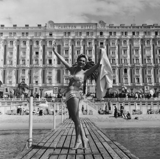 Eine Frau posiert im Bikini auf einem Steg vor dem Carlton Hotel in Cannes.