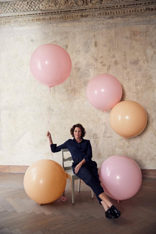 Eine Frau sitzt auf einem Stuhl, umgeben von großen, pastellfarbenen Ballons.