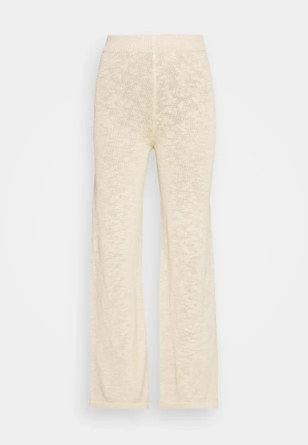 Eine lange, cremefarbene Strickhose vor einem weißen Hintergrund.