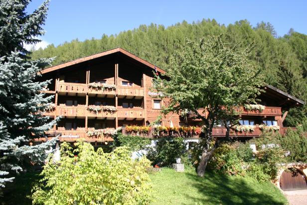 Ein hölzernes Hotel mit blühenden Blumenkästen vor einem bewaldeten Hügel.