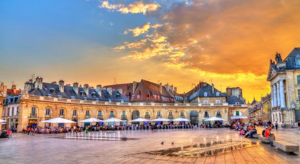 Der Place de la Libération in Dijon mit Menschen und einem Springbrunnen bei Sonnenuntergang.