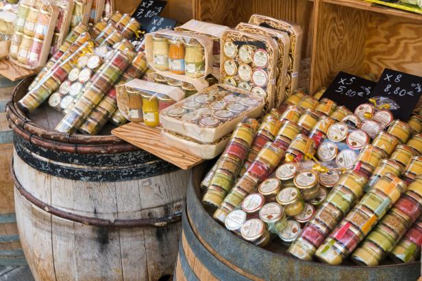 Auf zwei Holzfässern werden verschiedene Feinkostprodukte zum Verkauf angeboten.