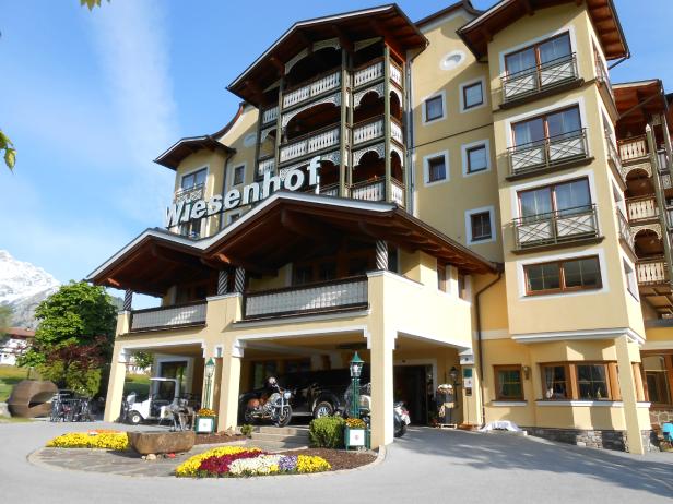 Das Hotel Wiesenhof mit seiner gelben Fassade und den hölzernen Balkonen an einem sonnigen Tag.