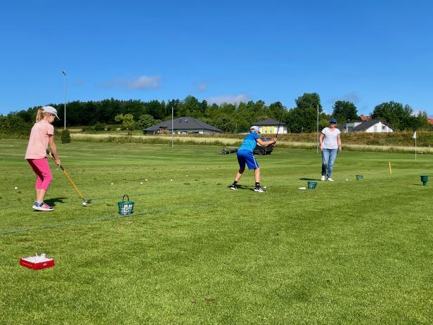 Kinder und eine Frau üben Golf auf einem sonnigen Golfplatz.