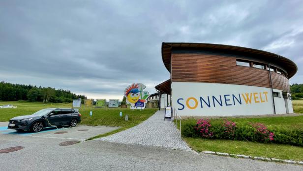 Ein Elektroauto lädt vor der „Sonnenwelt“ mit einem Smiley-Logo im Hintergrund.