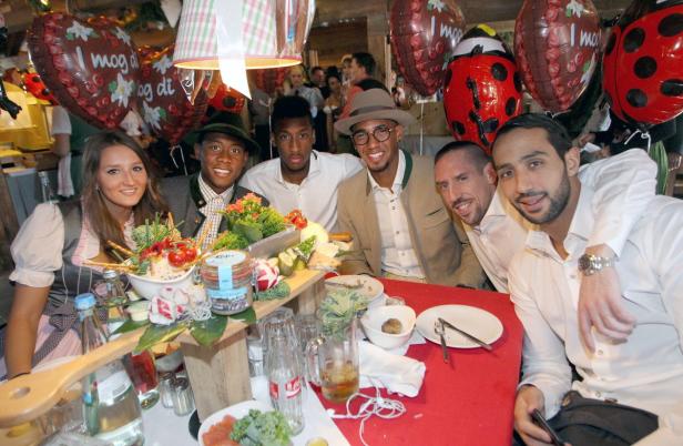 Eine Gruppe von Personen, darunter Fußballspieler, sitzt an einem Tisch mit Speisen und Getränken.