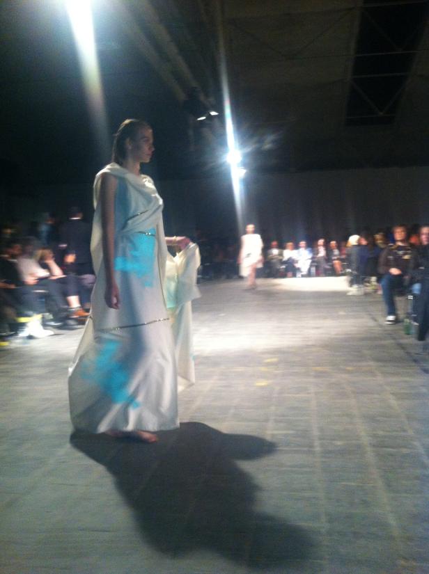 Eine Frau in einem weißen Kleid läuft über einen Laufsteg bei einer Modenschau.