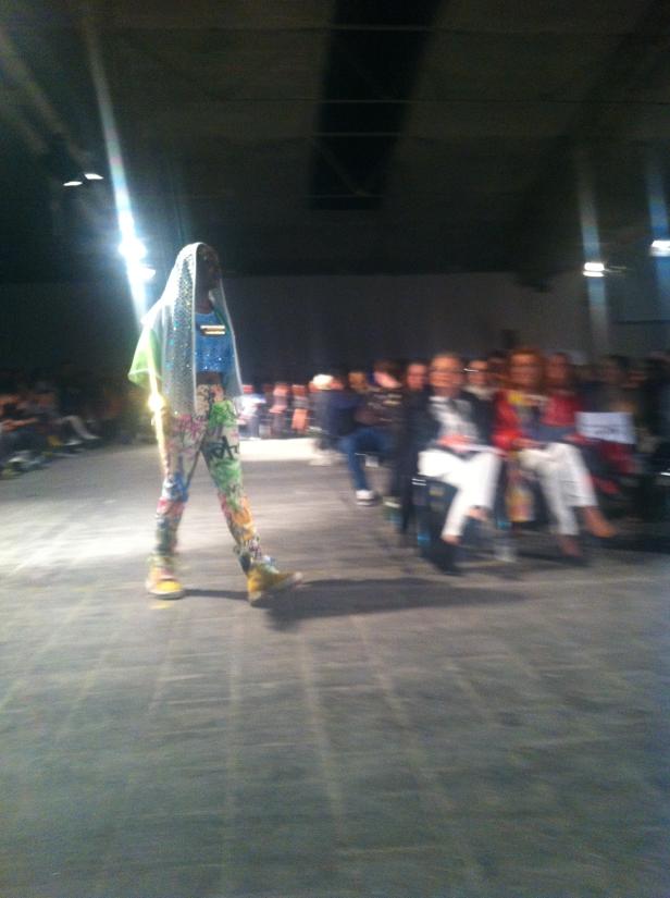 Ein Model läuft in farbenfroher Kleidung über einen Laufsteg.