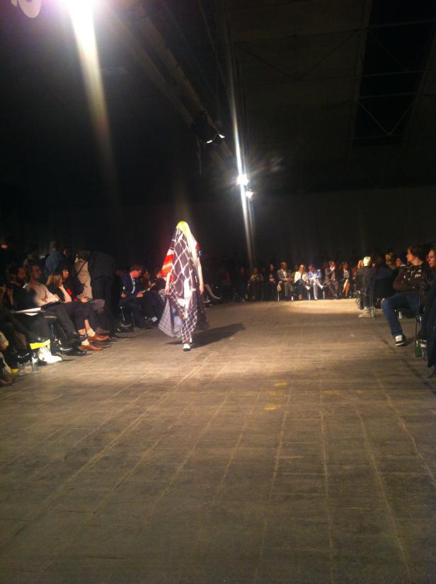 Eine Person in einem gemusterten Kleid läuft über einen Laufsteg bei einer Modenschau.