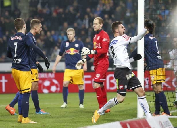 Ein Fußballspieler jubelt nach einem Tor, während andere Spieler im Hintergrund stehen.
