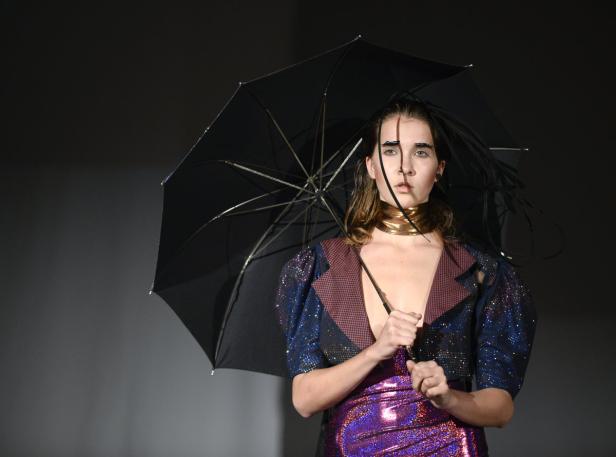 Eine Frau mit extravaganten Augenbrauen posiert mit einem schwarzen Regenschirm.