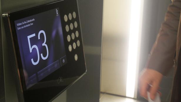 Ein Mann bedient ein digitales Bedienfeld, um den 53. Stock in einem Gebäude auszuwählen.