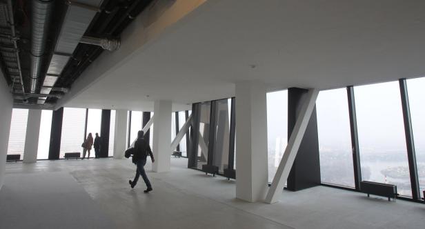 Eine Person geht durch einen offenen Raum mit großen Fenstern und Blick auf die Stadt.