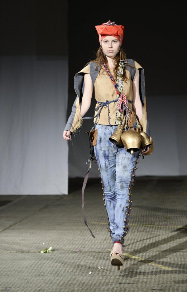 Eine Frau in ungewöhnlicher Kleidung mit Kuhglocken auf einem Laufsteg.