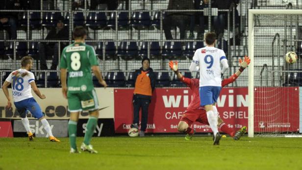 Ein Fußballspieler schießt den Ball auf das Tor, während der Torwart versucht, ihn abzuwehren.