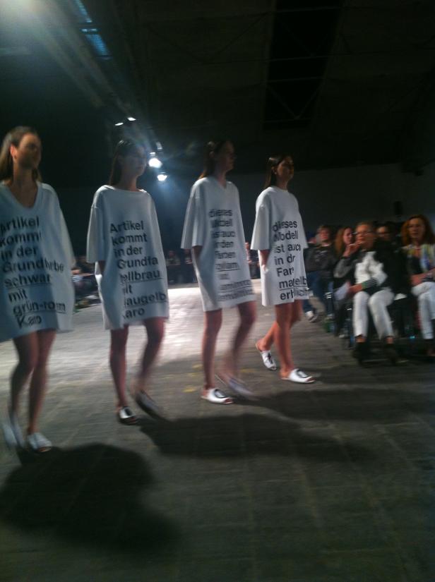 Models präsentieren Mode mit aufgedruckten Texten auf einem Laufsteg.