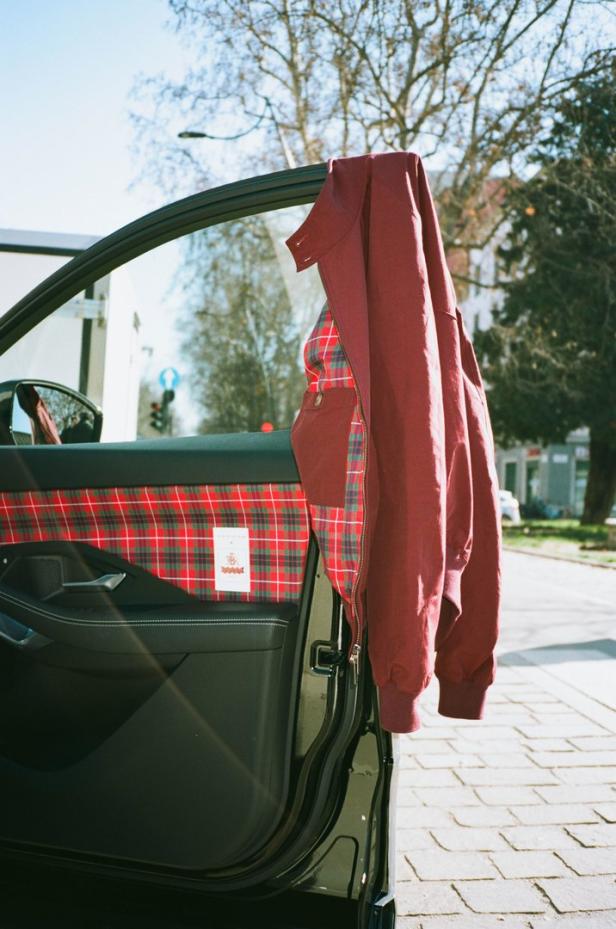 Eine offene Autotür mit rot karierter Innenverkleidung und einer darüber hängenden Jacke.