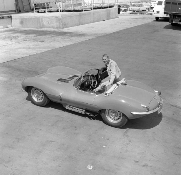 Steve McQueen sitzt auf einem hellen Jaguar D-Type Rennwagen.