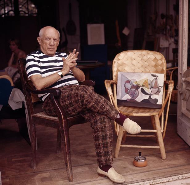 Pablo Picasso sitzt in einem Stuhl neben einem seiner Gemälde.