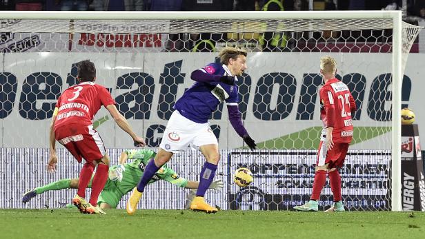 Ein Fußballspieler schießt den Ball ins Tor, während der Torwart versucht, ihn abzuwehren.