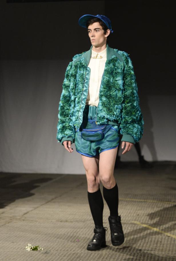 Ein Mann in einer blauen Jacke mit Blumenmuster und passender Mütze auf einem Laufsteg.