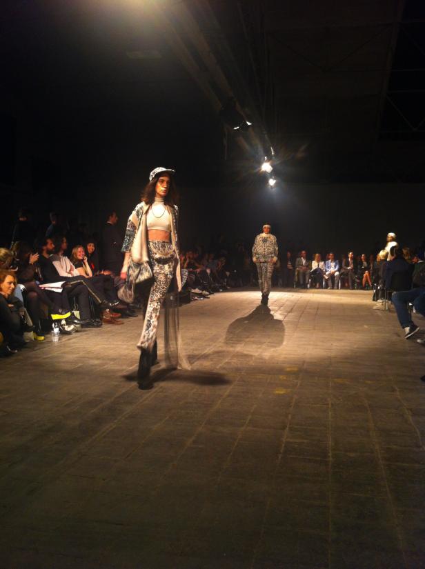 Zwei Models präsentieren Mode auf einem Laufsteg vor Publikum.