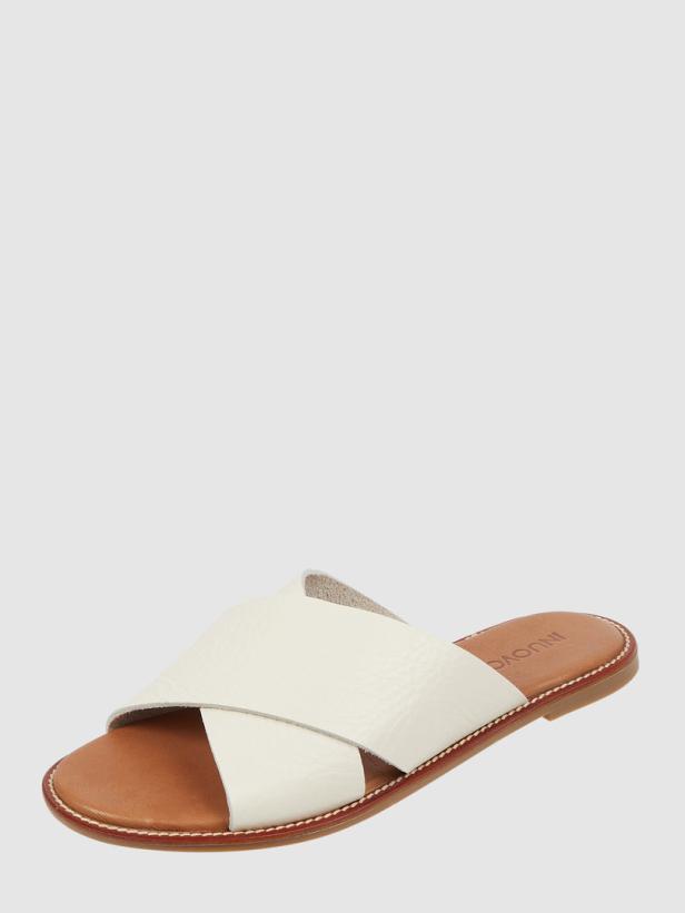 Ein weißer Lederslipper mit gekreuzten Riemen und brauner Sohle.