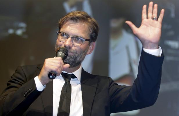 Jürgen Klopp spricht bei einer Veranstaltung in ein Mikrofon und hebt die Hand.