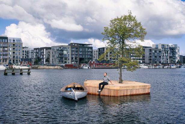 Ein Mann sitzt auf einer schwimmenden Plattform mit Baum, ein Boot liegt daneben.