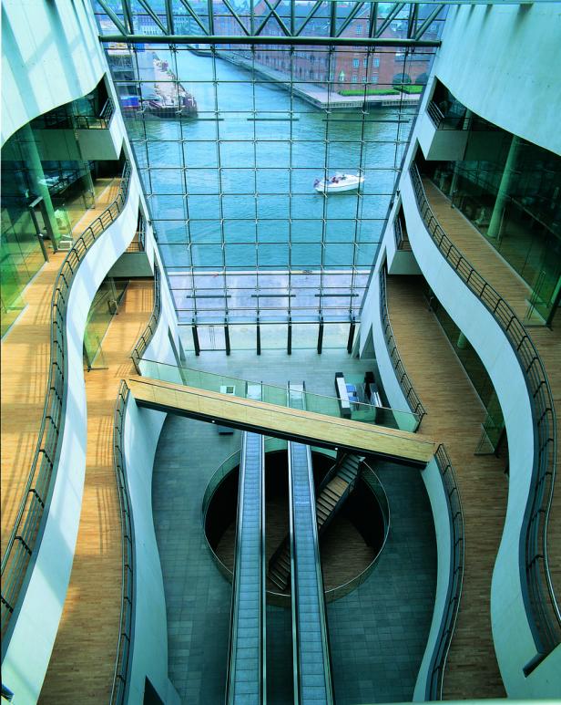 Blick von oben auf das Innere eines modernen Gebäudes mit Rolltreppen und Blick auf einen Kanal.