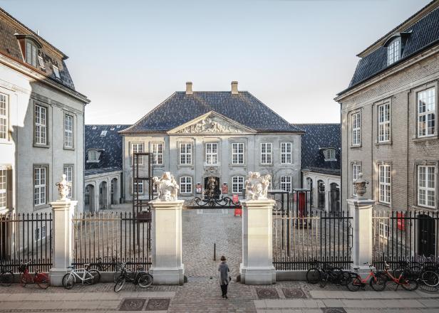 Eine Person betritt den Innenhof eines grauen, historischen Gebäudes in Kopenhagen.