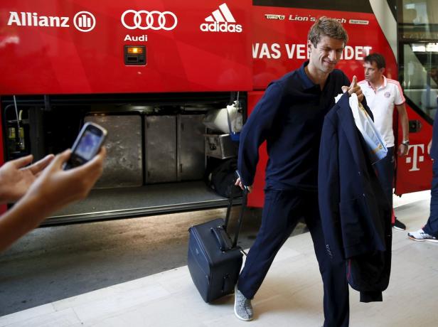 Thomas Müller steigt mit Koffer und Jackett aus einem Bus des FC Bayern München.