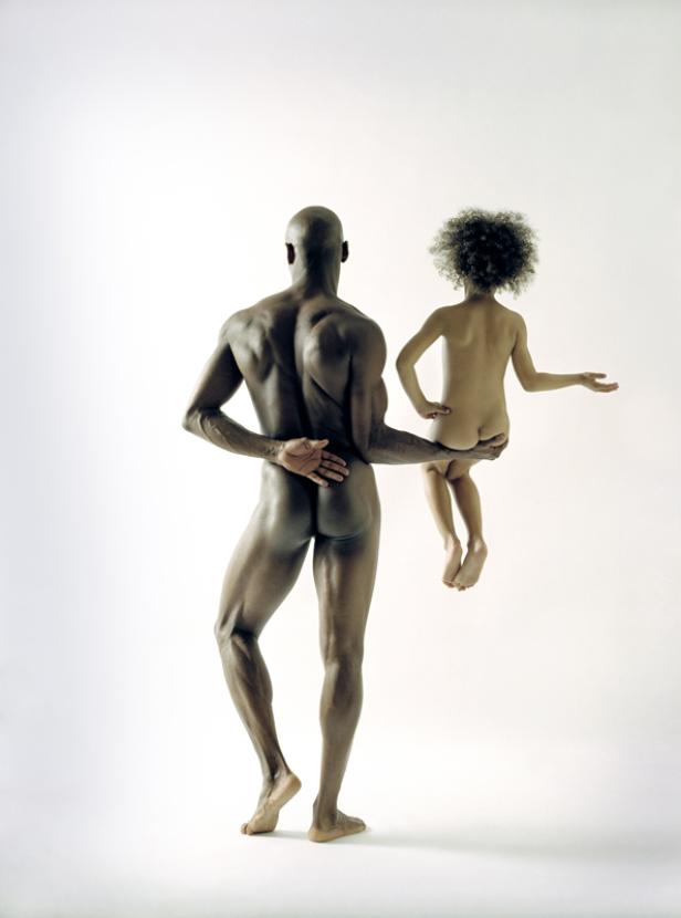 Ein Mann hält ein Kind im Arm, beide sind unbekleidet und stehen vor einem weißen Hintergrund.