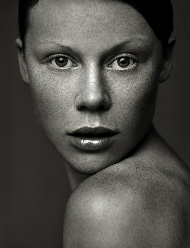 Schwarz-Weiß-Porträt einer Frau mit Sommersprossen, die über die Schulter blickt.