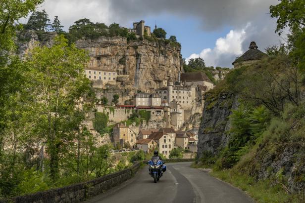 Ein Motorrad fährt auf einer Straße in Richtung des mittelalterlichen Dorfes Rocamadour.