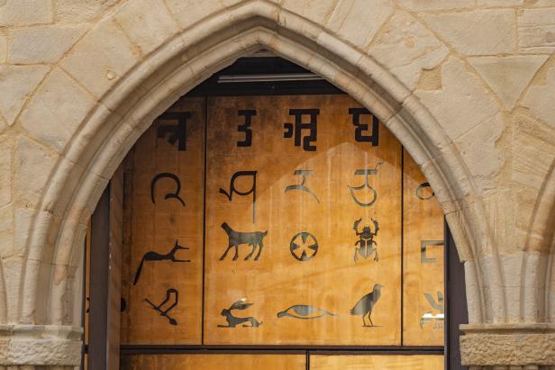 Ein Torbogen aus Stein mit einer Holztür, die mit Hieroglyphen und Schriftzeichen verziert ist.