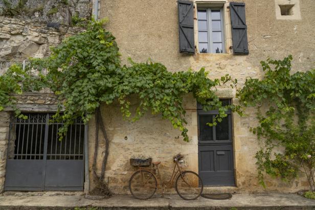 Ein rostiges Fahrrad lehnt an einer Steinmauer mit Weinreben.