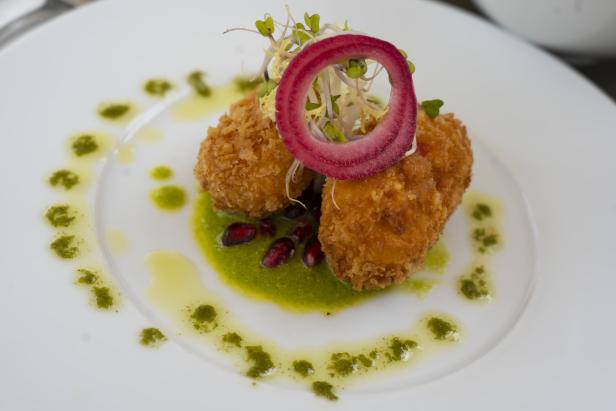 Frittierte Bällchen mit Zwiebelringen und Kräutern auf einem Teller mit grüner Soße.