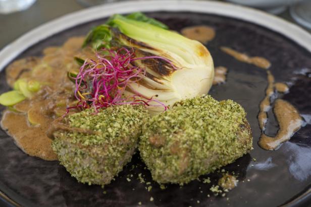 Ein Teller mit zwei Fleischstücken in grüner Kruste, Pak Choi und Soße.