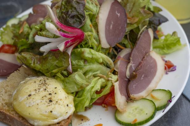 Ein Salatteller mit pochiertem Ei, Entenbrust und Gemüse garniert.