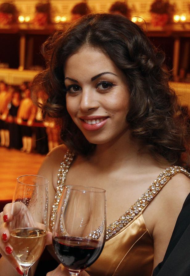 Eine Frau im goldenen Kleid hält zwei Gläser Wein in der Hand.
