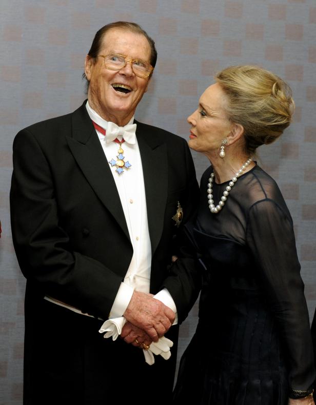 Roger Moore in Smoking und mit Orden, zusammen mit einer eleganten Dame.